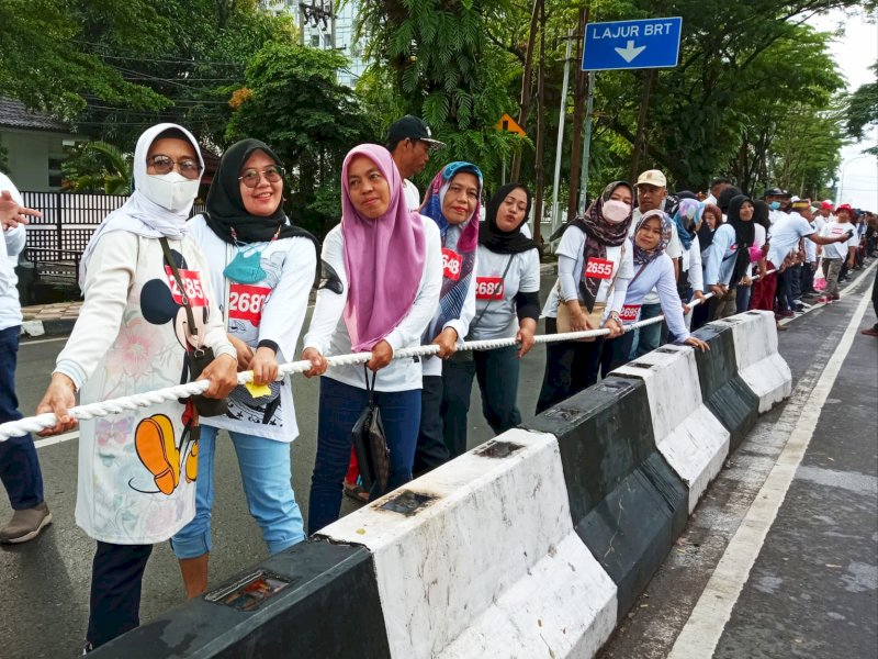 Peserta tarik rambang IKA Unhas Sulsel berada disamping pembatas jalan Jl. Jenderal Sudirman Makassar, Minggu (18/12/2022). (Foto: istimewa)