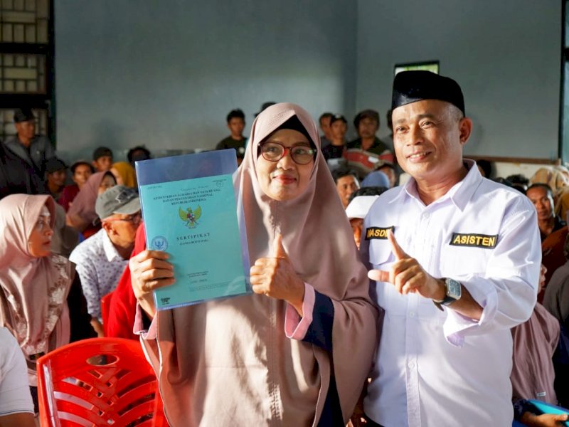 Penyerahan dilakukan secara simbolis oleh Asisten II Bidang Perekonomian dan Pembangunan, Masdin, sertifikat tanah warga di Aula Desa Libukan Mandiri, Kecamatan Towuti, Sabtu (18/10/2025). @Jejakfakta/dok. ikp-humas/kominfo-sp