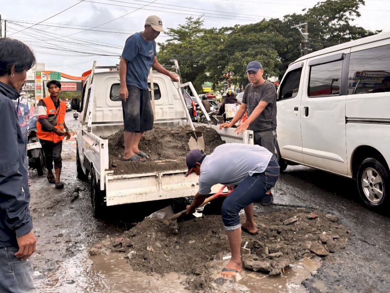 Warga gotong royong menimbun jalan berlubang dangan pasir di jalan Aroepala Makassar, Sabtu (15/11/2025). @jejakfaktacom/istimewa